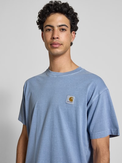 Männermodel trägt T-Shirt mit Label-Detail Modell 'Nelson' von Carhartt Work In Progress aus reiner Baumwolle in Hellblau, Nahaufnahme Oberkörper.