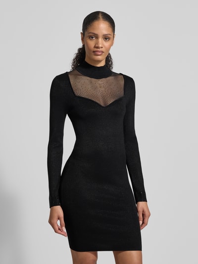 Frauenmodel trägt Slim Fit Kleid aus Viskose-Mix mit Ziersteinbesatz Modell 'Lucy' von Guess, semitransparent, langärmelig, Stehkragen, Ganzkörperansicht von vorne.