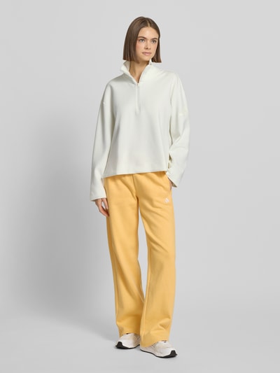 Modelka kobieca nosi Pullover mit Stehkragen und Reißverschluss od adidas Sportswear, biały, z poliestru, luźny krój, logo, widok całej sylwetki z przodu.