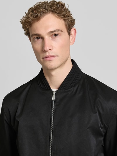 Männermodel trägt Regular Fit Blouson von BOSS in Schwarz, Optik: Unifarben, Reißberschluss, seitliche Eingrifftaschen, Nahaufnahme Oberkörper.