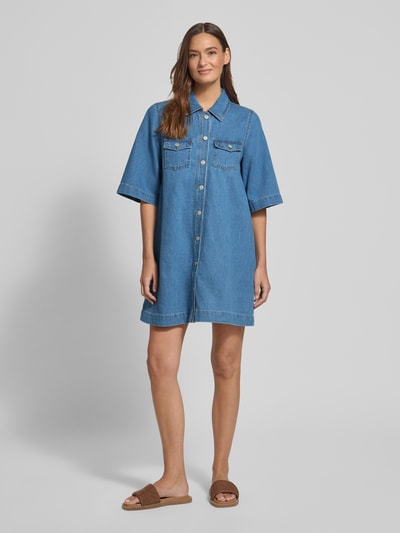 Frauenmodel trägt Jeanskleid mit Brusttaschen Modell 'Mira' von mbyM, Reine Baumwolle, Relaxed-Fit Minikleid, Hemdblusenkragen, Knopfleiste, mittlere Blautöne, glatte Textur, Ganzkörperansicht von vorne.