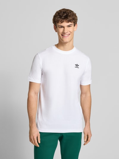 Männermodel trägt T-Shirt mit Label-Stitching von adidas Originals in Weiß, reine Baumwolle, Regular Fit, Rundhals, Ganzkörperansicht von vorne.