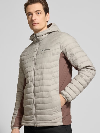 Männermodel trägt Gewatteerd jack met capuchon en logoprint van Columbia, regular fit, ritssluiting, ruglengte maat M 72 cm, schouderbreedte 47 cm, borstwijdte 52 cm, mouwlengte 69 cm, lichte en bruine tinten, horizontale stiksels, zachte textuur, Ganzkörperansicht van voren.