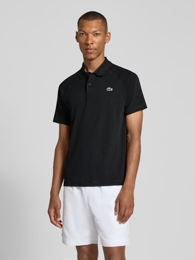 Męski model nosi czarne Regular Fit Sport-T-Shirt mit Polokragen von Lacoste, gładki materiał, białe szorty, Ganzkörperansicht von vorne, Herren Sport-T-Shirt von Lacoste Sport.