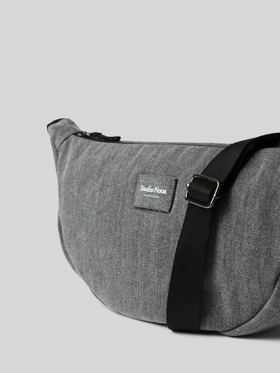 Produktfoto, Pouch aus reiner Baumwolle in Denim-Optik von Studio Noos, grauer Stoff mit feiner Webstruktur, Logo-Detail, schwarzer Riemen, Hauptfach mit Reißverschluss, Maße ca. 40x20x10 cm, schlichte Farbgebung