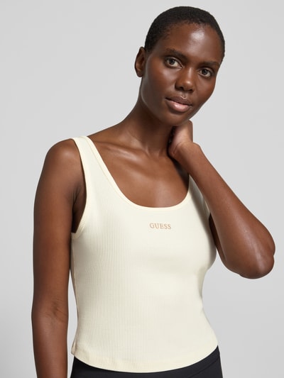 Modelka kobieca nosi Slim Fit Top mit Logo-Stitching Modell 'Circe' od Guess Activewear z bawełnianą mieszanką, krój slim fit, jasny kremowy kolor, okrągły dekolt, delikatna faktura materiału, długość tyłu w rozmiarze S: 29 cm, zbliżenie na górną część ciała, widok z przodu.