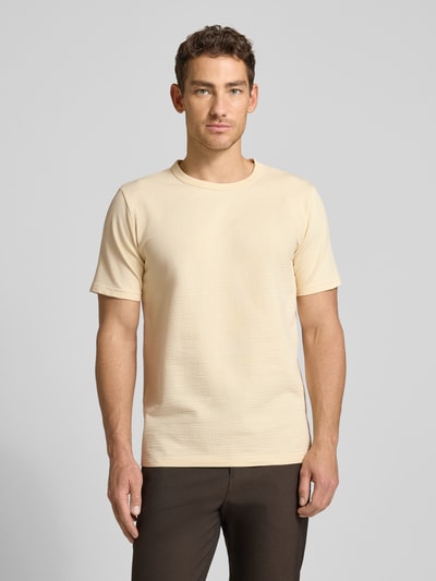 Männermodel trägt Regular Fit T-Shirt aus Baumwoll-Mix Modell 'SANDER' von SELECTED HOMME in Beige, Seersucker-Struktur, Ganzkörperansicht von vorne.