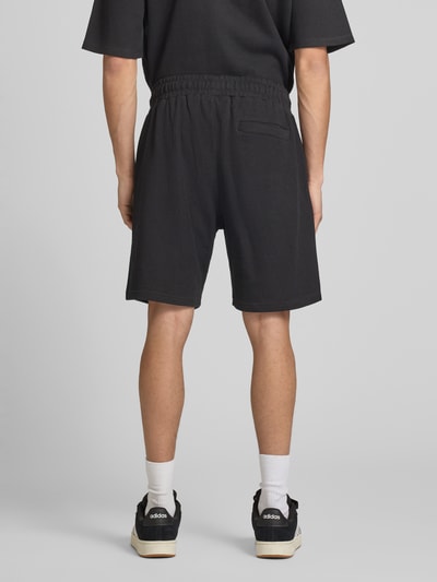 Männermodel trägt Shorts mit Logo-Stitching und elastischem Bund von Pegador in Schwarz, Reine Baumwolle, Loose-Fit, Feinripp, Gesäßtasche, Ganzkörperansicht Rückansicht