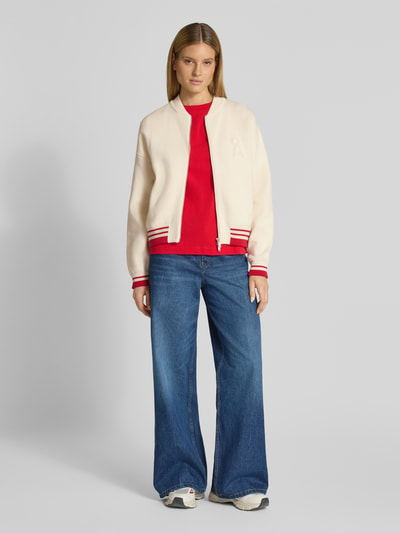 Frauenmodel trägt Oversized Bomberjacke aus Baumwoll-Mix mit Woll-Anteil Modell 'ICONIC A' von Armedangels, cremefarben, College-Kragen, unifarben, Zweiwege-Reißverschluss, Logo-Stitching, lange Ärmel, Rippstrick, kombiniert mit blauer weiter Jeans, Ganzkörperansicht von vorne.