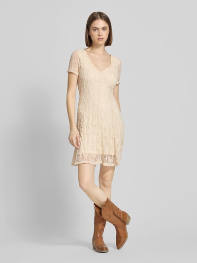 Frauenmodel trägt Slim Fit Minikleid aus Spitze Modell 'ALBINA' von Only in Beige mit V-Ausschnitt, Kurzarm, Spitzenmuster, Ganzkörperansicht von vorne.