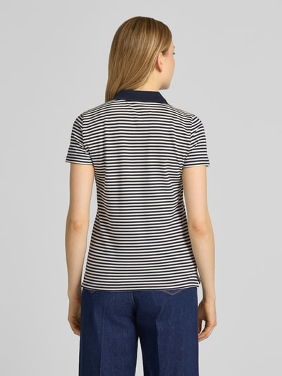 Modelka nosi Regular Fit Poloshirt aus Baumwoll-Mix von Tom Tailor, efekt: wzór w paski na całej powierzchni, krótki rękaw, kołnierzyk polo, dekolt w serek, listwa guzikowa, wyhaftowany motyw, wykończenie materiału: pika, mieszanka bawełny, widok całej sylwetki z tyłu.