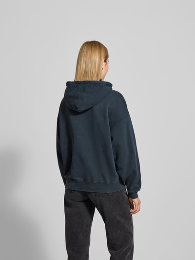 Frauenmodel trägt Oversized Hoodie mit Logo-Stitching von Anine Bing in Dunkelblau, reine Baumwolle, Känguru-Tasche, elastische Abschlüsse, Oversized-Fit, Rückenlänge bei Größe S 63 cm, Ganzkörperansicht Rückansicht.