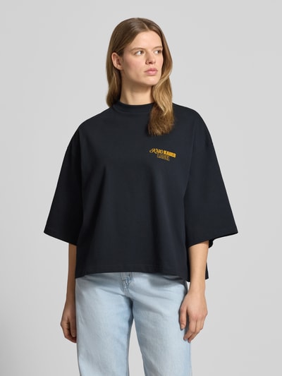 Frauenmodel trägt Cropped T-Shirt mit rückseitigem Statement-Print von Karo Kauer, Damen T-Shirt aus Reine Baumwolle in Loose-Fit, Logo-Print, Gerippter Rundhalsausschnitt, Überschnittene Schultern, Farbe Schwarz, Modell 'No Hustle', Rückenlänge Größe S 60 cm, Nahaufnahme Oberkörper.