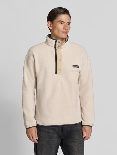 Männermodel trägt Fleecepullover mit Label-Patch Modell 'Helvetia™ II' von Columbia in Beige mit Stehkragen und Brusttasche, Ganzkörperansicht von vorne, gerader Schnitt, Material mit weicher Struktur, KI-modifiziertes Bild.