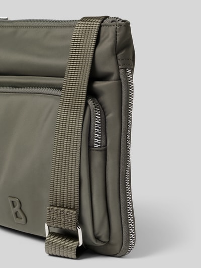 Produktfoto, olivgrüne Handtasche mit Label-Detail Modell 'verbier play 1.0 serena' von BOGNER, glatte Textur, robuste Kanten, Reißverschluss und verstellbarer Schulterriemen, Größe 25x25x4 cm, Schulterriemen 105 cm.