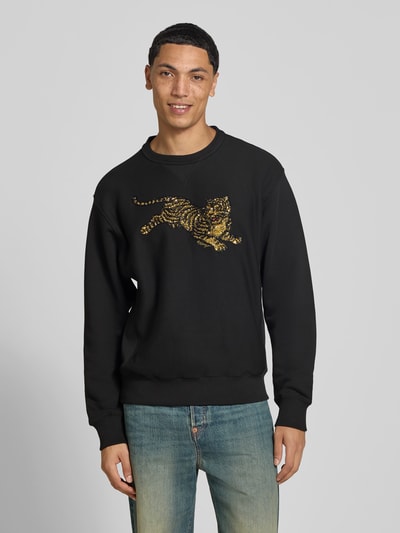 Mannelijk model draagt Sweatshirt aus reiner Baumwolle van Kenzo, zwart met pailletten motiefprint, recht pasvorm, opstaande kraag, ribboorden, puur katoen, ruglengte maat M 66 cm, geheellichaamsaanzicht van voren.