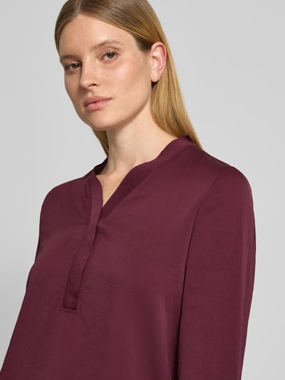 Kobiece model prezentuje Regular Fit Bluse mit V-Ausschnitt von Marc Cain, krój regular fit, dekolt w serek, detal z logo, bluzka w kolorze bordowym, długość tyłu w rozmiarze 36: 65 cm, długość rękawów w rozmiarze 36: 59 cm, zbliżenie na górną część sylwetki