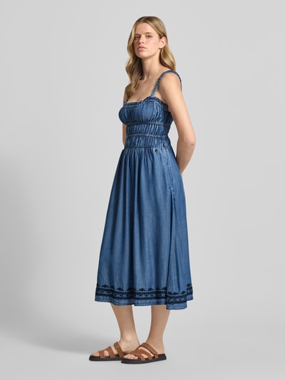 Vrouwenmodel draagt Tailliertes Jeanskleid aus Lyocell van Pepe Jeans in denimlook met getailleerd model, midilengte, vierkante hals, kwastdetails, borduursels, elastische borstbanden, naadritssluiting, tunnelkoord, smalle bandjes, materiaal lyocell. Ganzkörperansicht van voren.