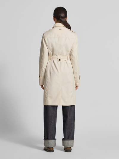 Modelka nosi Regular Fit Trenchcoat aus Baumwoll-Mix od s.Oliver RED LABEL, jasny kolor, bawełniany twill, pasek, szlufki, długi rękaw, naszywka z logo, tylne karczek, boczne kieszenie, widok całej sylwetki od tyłu.