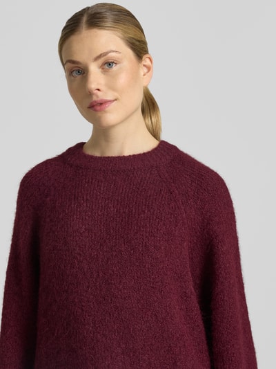 Vrouwenmodel draagt Strickpullover mit Raglanärmeln van FREE/QUENT in bordeauxrood, rechte fit, ronde hals, materiaal met wol, nahaufnahme bovenlichaam.