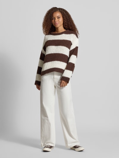 Kobiece model nosi sweter Relaxed Fit Pullover im Chunky Knit Look model 'DORTHEA' od PIECES, kremowo-brązowe pasy, dzianina, szerokie rękawy, szerokie nogawki, widok całej sylwetki z przodu, sweter damski PIECES.