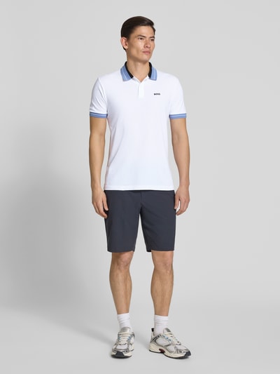 Männermodel trägt Regular Fit Poloshirt aus Baumwoll-Mix Modell 'PL_Member' von BOSS Green in Weiß mit blauen Kontraststreifen, gerippte Abschlüsse, Label-Schriftzug, Piqué-Struktur, Ganzkörperansicht von vorne.