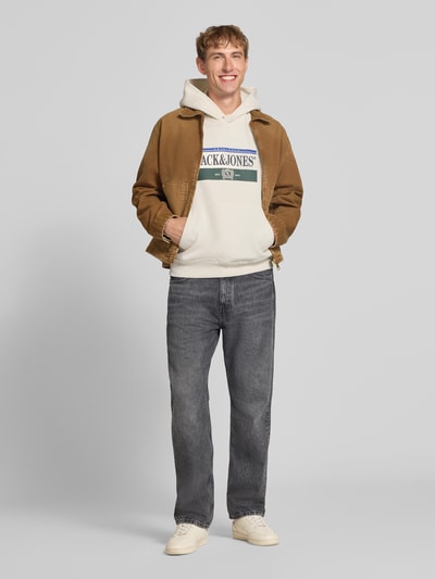 Männermodel trägt Hoodie mit Label-Print Modell 'FREDERIKSBERG' von JACK & JONES in Beige, lockerer Schnitt, Ganzkörperansicht von vorne. Baumwoll-Mix, Kapuze, Kängurutasche, gerippte Abschlüsse.