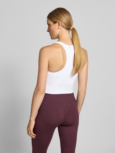 Frauenmodel trägt Slim Fit Top mit integriertem Bustier Modell 'Anywhere' von Fabletics, weißer elastischer Material-Mix, Ganzkörperansicht Rückansicht.