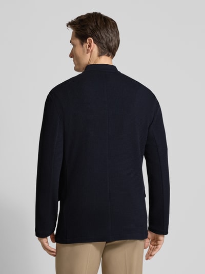 Männermodel trägt Slim Fit Sakko mit Stehkragen und Pattentaschen von Emporio Armani, dunkle Farbe, Material-Mix mit Viskose-Anteil, Ganzkörperansicht Rückansicht.