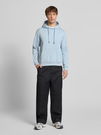 Männermodel trägt Hoodie mit Kapuze Modell 'BRADLEY' von Jack & Jones in Hellblau, Känguru-Tasche, lockerer Schnitt, Ganzkörperansicht von vorne.