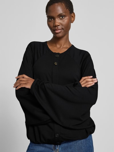 Frauenmodel trägt Oversized Cardigan aus Lyocell-Mix von black palms in Schwarz mit Rundhalsausschnitt, durchgängiger Knopfleiste und elastischen Abschlüssen, Oversized-Fit, Rückenlänge 58 cm bei Größe S/M, Nahaufnahme Oberkörper.