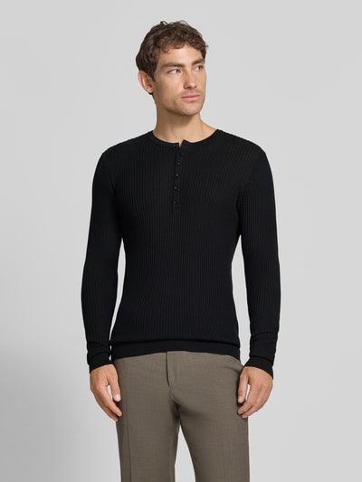 Männermodel trägt Strickpullover aus Lyocell-Woll-Mix mit Knopfleiste von Antony Morato, Slim Fit, Ripp-Optik, schwarze Farbe, Ganzkörperansicht von vorne.
