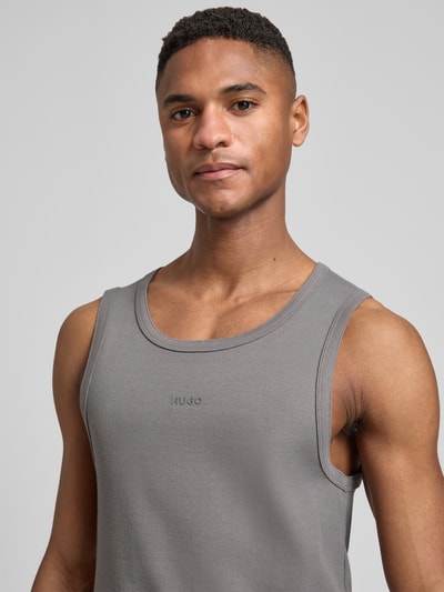 Männermodel trägt Slim Fit Tank Top aus Baumwoll-Mix Modell 'DAPOTA' von HUGO in Grau, Feinripp, Label auf Brust, Nahaufnahme Oberkörper.