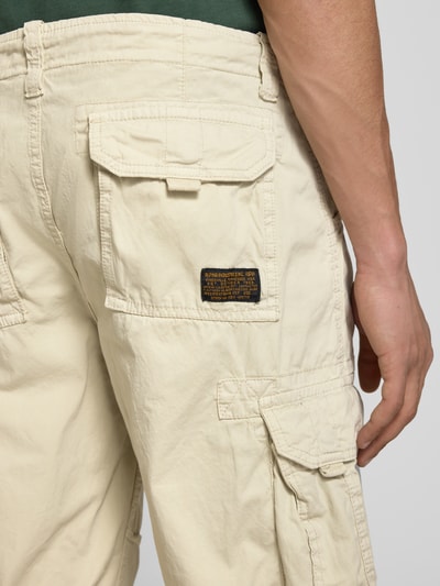 Mężczyzna nosi Bermudas mit Pattentaschen und Logo-Stitching od Alpha Industries, beżowa bawełna, krój straight fit, detaile szwów i naszywek, zbliżenie tylnej części.