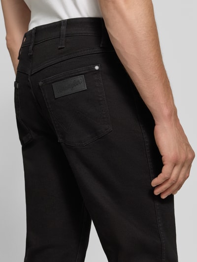 Männermodel trägt Tapered Fit Jeans aus Baumwoll-Mix Modell 'Redford' von Wrangler in Schwarz, strukturierte Oberfläche, Ganzkörperansicht Rückansicht. Herren Tapered Fit Jeans von Wrangler.