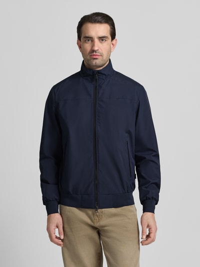 Mannenmodel draagt Regular Fit Jacke mit Stehkragen Modell 'Finlay' van SAVE THE DUCK in donkerblauw, met elastische boorden, zichtbare ritssluiting en steekzakken, context: heren jack, zweiwegereißverschluss, regular fit, lengte rug maat M 69 cm, schouderbreedte 46 cm, borstwijdte 60 cm, mouwlengte 68 cm. Volledige lichaamsweergave van voren.