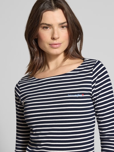 Modelka kobieca ma na sobie Regular Fit 3/4-Shirt aus Baumwoll-Mix od Tom Tailor, materiał w bawełnianym miksie, wzór w paski, napis z przodu, dekolt typu łódka, rękaw 3/4, kolor granatowo-biały, allover-motyw, widok z przodu, zbliżenie na górną część ciała.