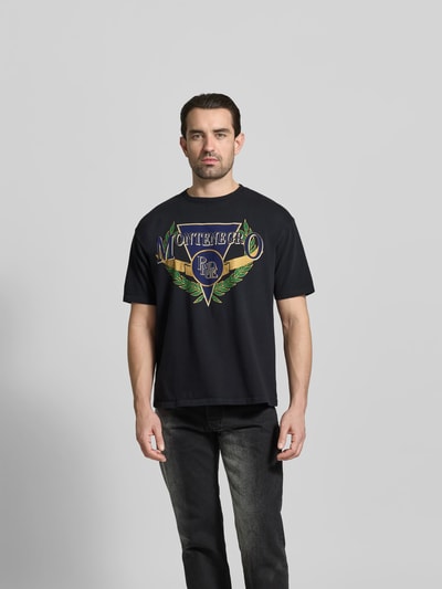 Männermodel trägt Regular Fit T-Shirt mit Logo-Print von RHUDE in Schwarz, reine Baumwolle, Rundhalsausschnitt, Rückenlänge 68 cm, Ganzkörperansicht von vorne.