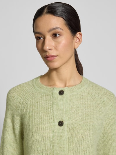Vrouwenmodel draagt Regular Fit Strickjacke aus Woll-Mix mit Alpaka-Anteil Modell 'LULU' van Selected Femme, unikleuren structuur breisel, ronde hals, lange raglanmouwen, eenrijige knoopsluiting, detailopname bovenlichaam.