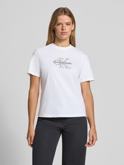 Frauenmodel trägt Regular Fit T-Shirt aus reiner Baumwolle von Calvin Klein Jeans in Weiß, leicht strukturierte Oberfläche, Ganzkörperansicht von vorne.