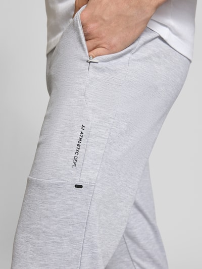 Männermodel trägt Sweatpants mit Baumwoll-Anteil Modell 'GORDON' von Jack & Jones in hellgrau mit seitlicher Reißverschlusstasche, Nahaufnahme Oberschenkel.