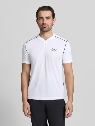Männermodel trägt Regular Fit T-Shirt mit Stehkragen von EA7 Emporio Armani in Weiß mit Label-Print, Reißverschluss, Ganzkörperansicht von vorne.