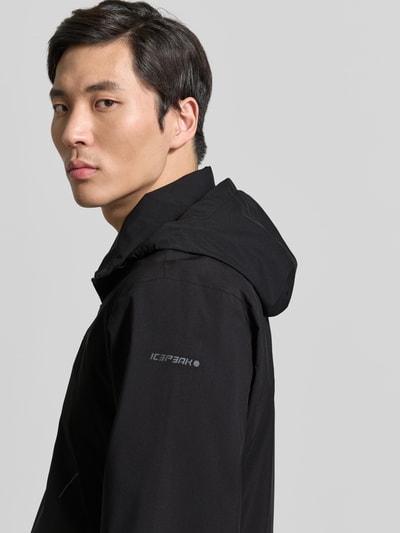 Męski model nosi kurtkę z kapturem model 'BROCTON' od Icepeak, czarna, krój regular fit, zamek błyskawiczny, widoczne logo na ramieniu, zdjęcie w zbliżeniu na górną część ciała z przodu, długość tyłu w rozmiarze 50: 65 cm, szerokość ramion w rozmiarze 50: 49 cm, szerokość klatki piersiowej w rozmiarze 50: 57 cm, długość rękawów w rozmiarze 50: 67 cm