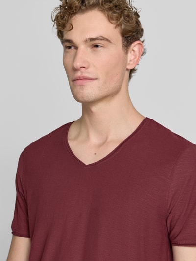 Mężczyznamodel nosi t-shirt z dekoltem w serek i zrolowanym brzegiem od MCNEAL, bawełna, krój regular fit, długość tyłu w rozmiarze M: 81 cm, zbliżenie na górną część ciała.