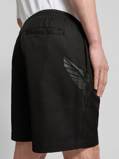 Männermodel trägt Shorts mit Logo und elastischem Bund von COLUCCI in Schwarz mit Eingrifftaschen, Regular-Fit, Ganzkörperansicht Rückansicht.