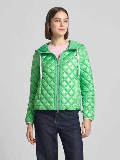 Frauenmodel trägt Regular Fit Jacke in Stepp-Optik Modell 'YOSIE' von Frieda & Freddies in glänzendem Grün mit Kapuze, Eingrifftaschen, Reißverschluss, Logo-Applikation, elastischen Ärmelabschlüssen, Ganzkörperansicht von vorne.