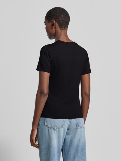Frauenmodel trägt schwarzes T-Shirt aus Viskose-Elasthan-Mix mit Logo von Guess Activewear, kombiniert mit hellblauer Jeans, Ganzkörperansicht Rückansicht.