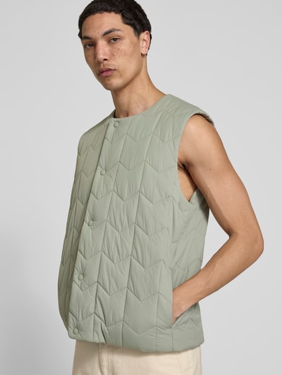 Männermodel trägt Regular Fit Weste in Stepp-Optik von MAISON KITSUNÉ in hellem Grün mit Knopfleiste und Eingrifftaschen, Nahaufnahme Oberkörper.
