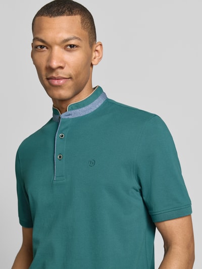 Männermodel trägt Regular Fit Poloshirt mit Stehkragen und Logo-Stitching von bugatti in Grün aus Reine Baumwolle, Nahaufnahme Oberkörper. Rückenlänge bei Größe M: 70 cm, kurze Knopfleiste, Label-Detail.