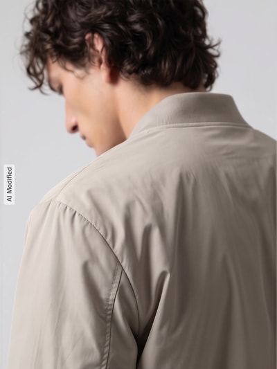 Männermodel trägt Regular Fit Bomberjacke mit Baseball-Kragen Modell 'CHARLES' von Selected in Beige, glatte Textur, Rückansicht, KI-modifiziertes Bild. Herren Bomberjacke / Blouson von Selected.